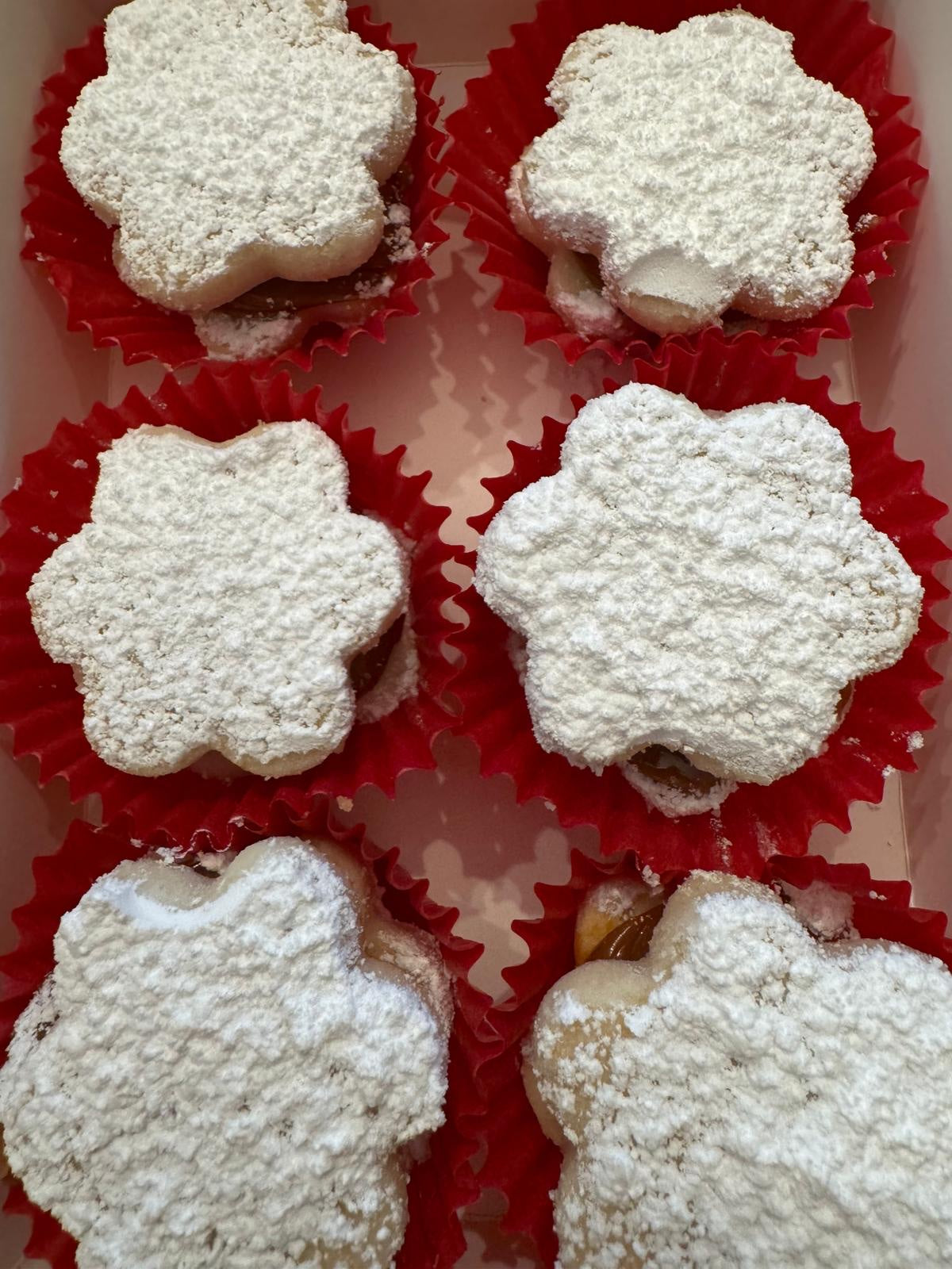 Flower-shaped Traditional alfajores with powdered sugar in red paper cups.